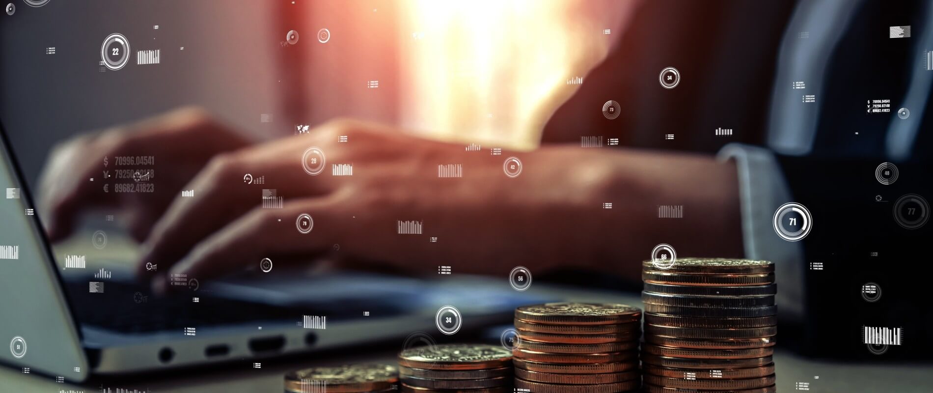 Close-up of a person typing on a laptop with stacked coins in the foreground